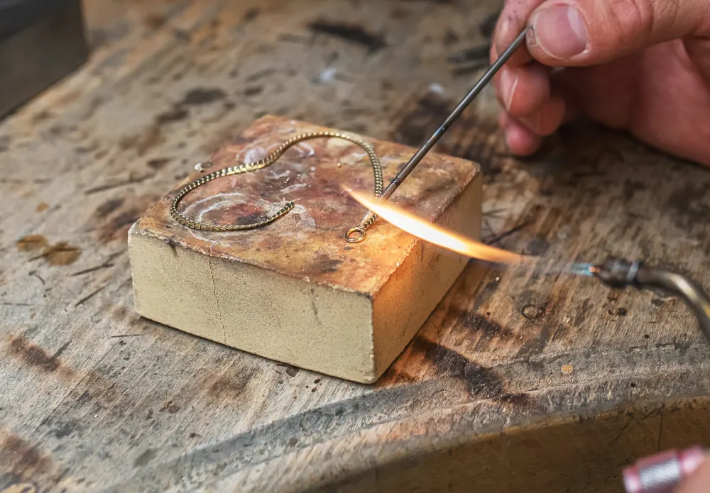 Goldschmiedin lötet eine Goldkette mit offener Flamme